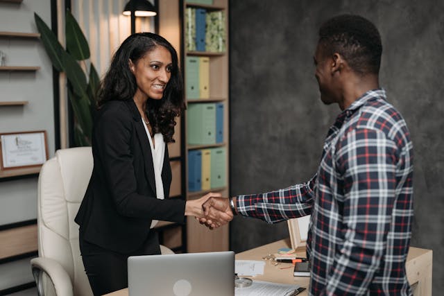 woman in suit shaking hands with man over desk